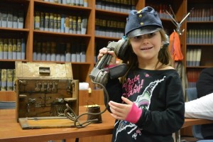 Child wearing a WW1 cap, plays with a WW1 telephone