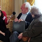 A woman interviews an elderly couple, they are all laughing