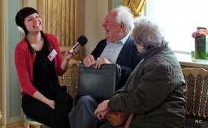 A woman interviews an elderly couple, they are all laughing